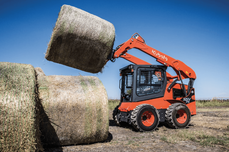 Skid steer lifting a large hay bale
