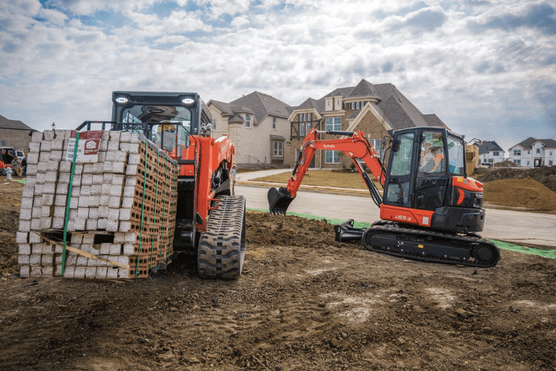 A loader moving a pallet of bricks and an excavator digging
